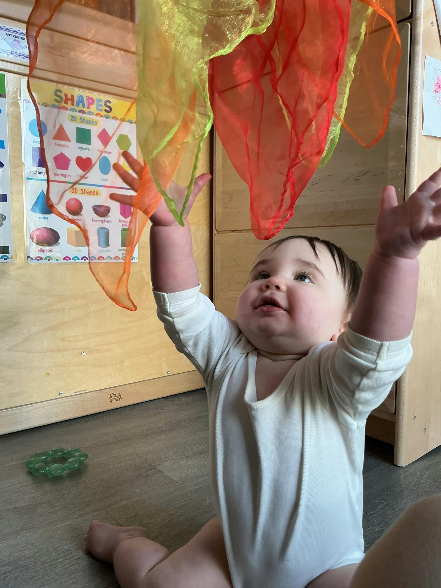 A child reaching up toward colorful scarves in a classroom