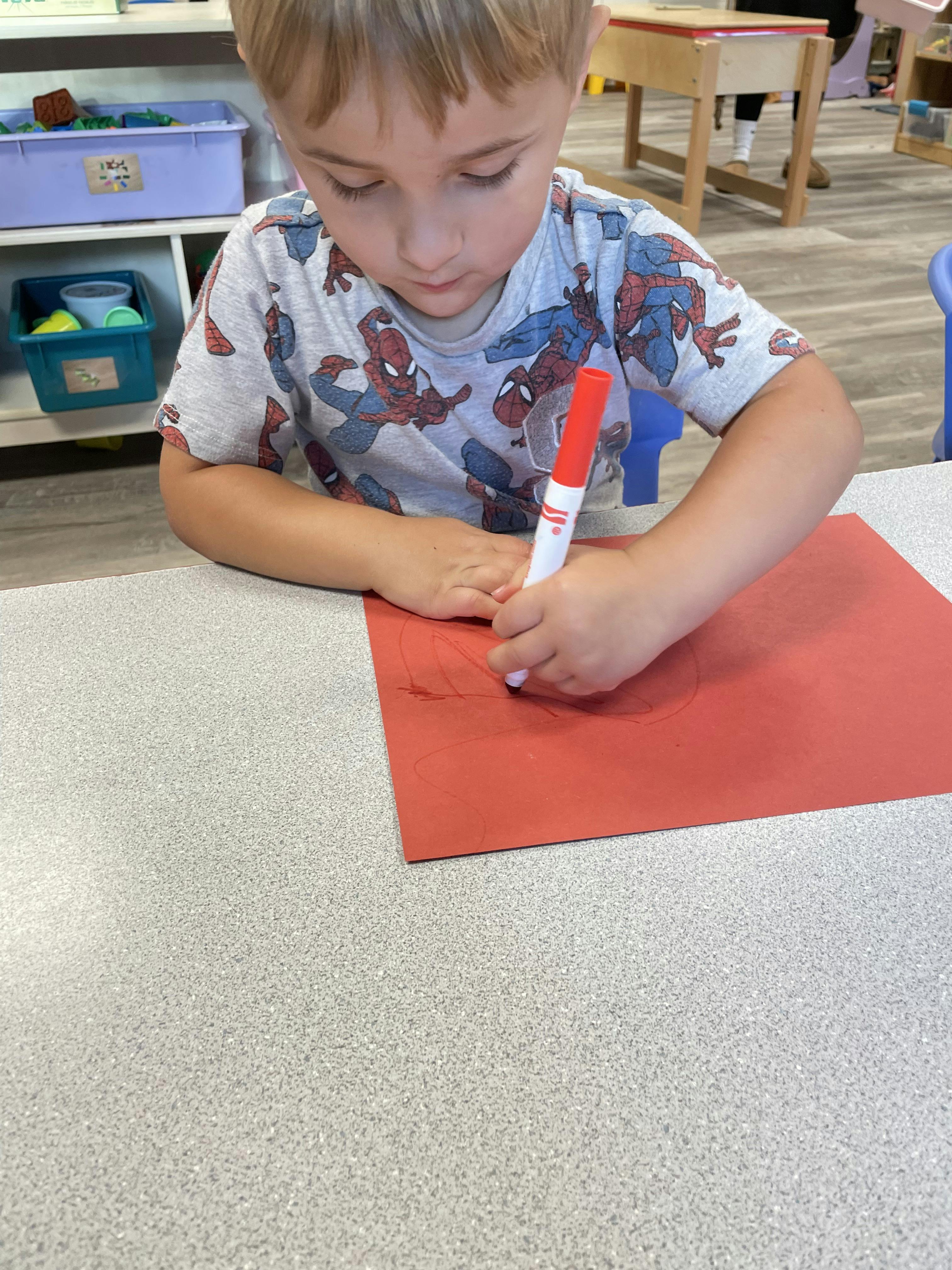 Child drawing on red paper with a marker