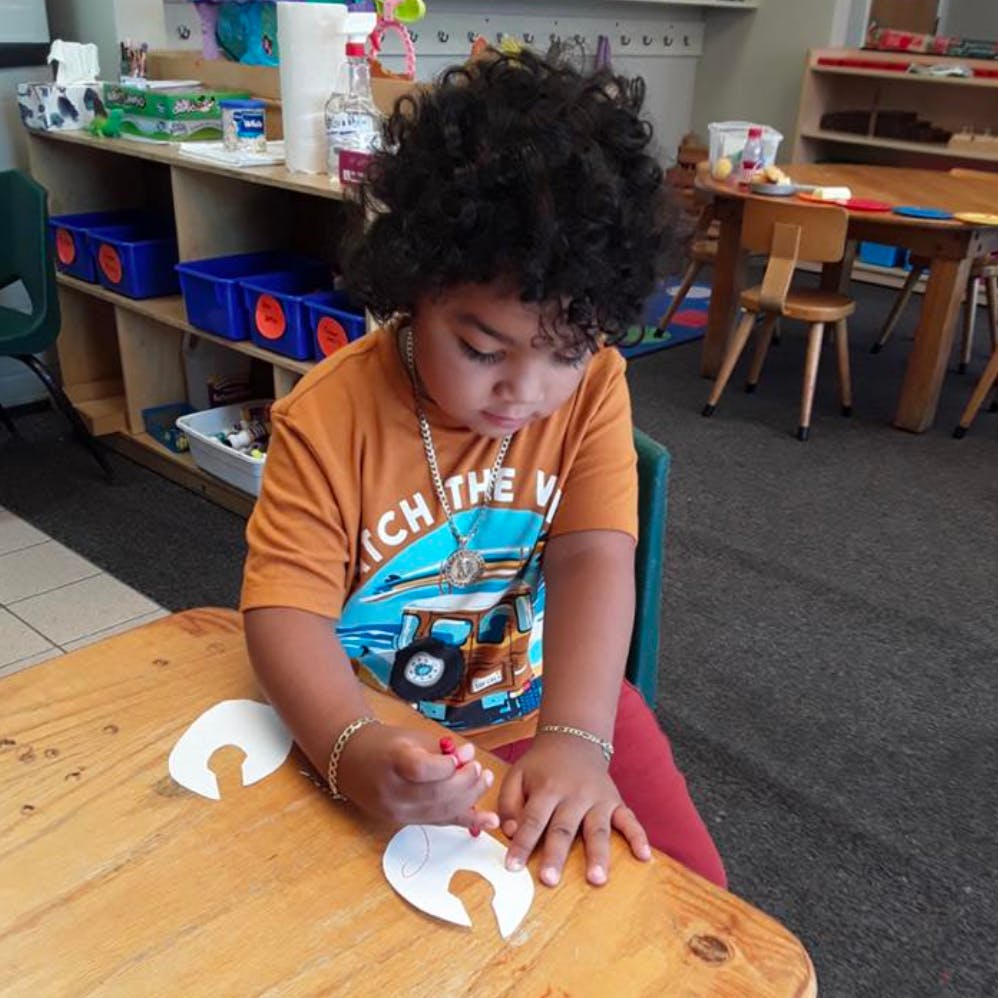 Child drawing on paper cutouts at a table in a classroom