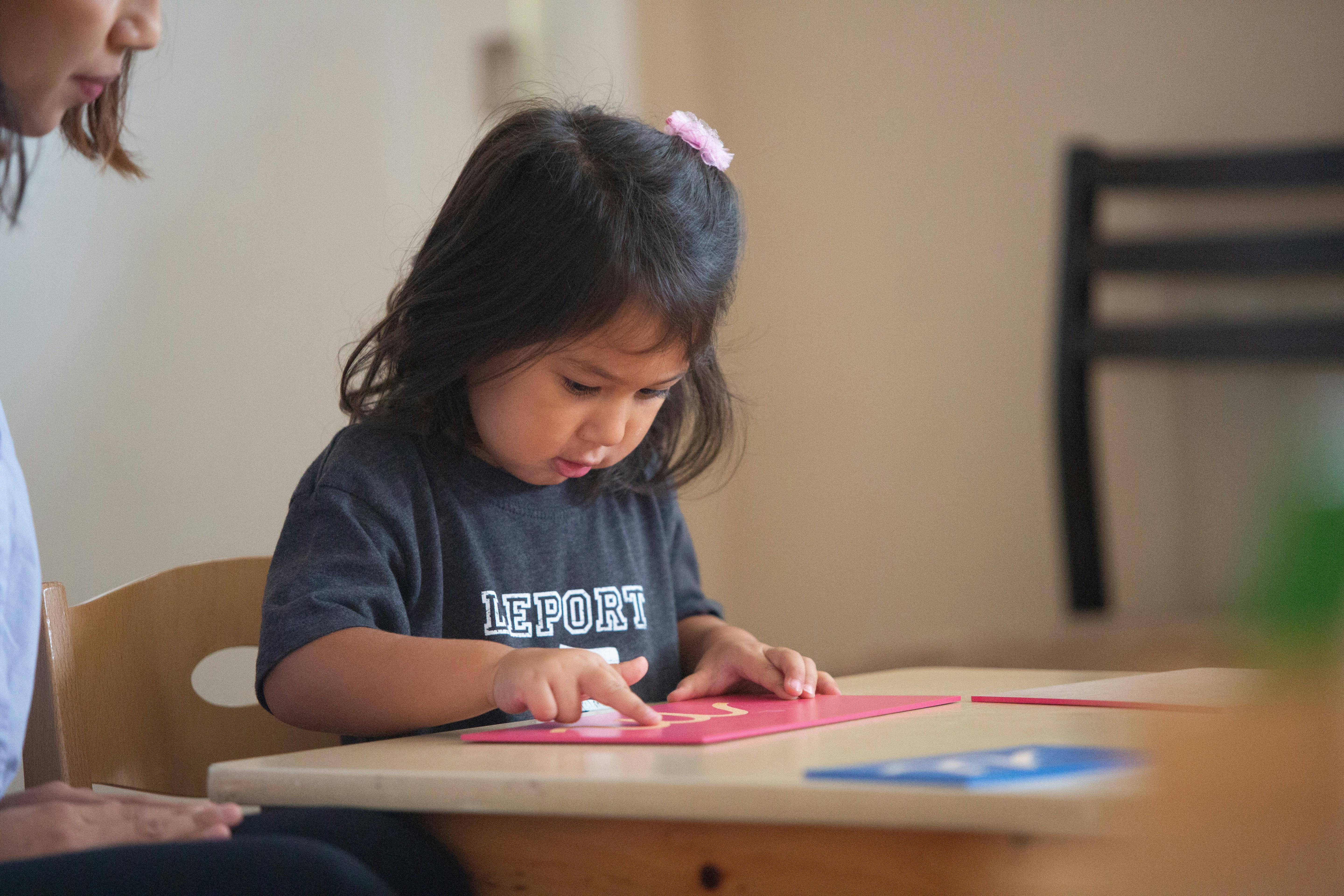 Child pointing at a red card on a table with a person next to them