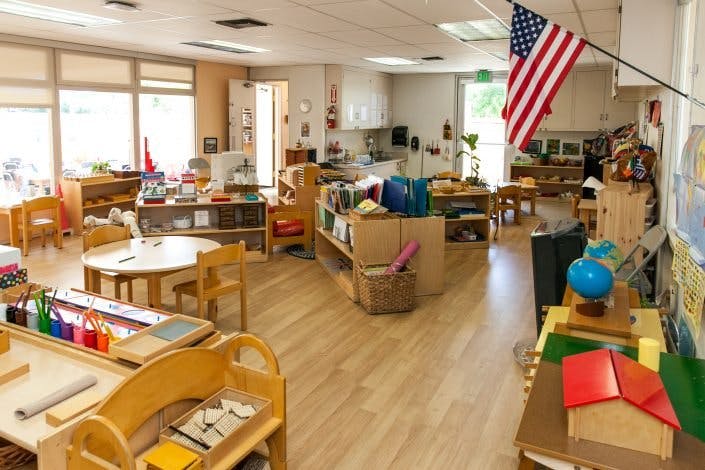 Classroom with tables, chairs, shelves, and an American flag