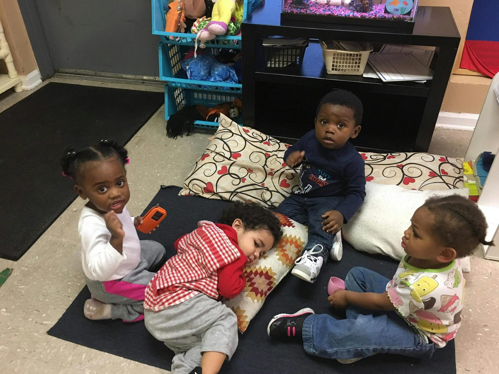 Four children sitting and lying on pillows on the floor