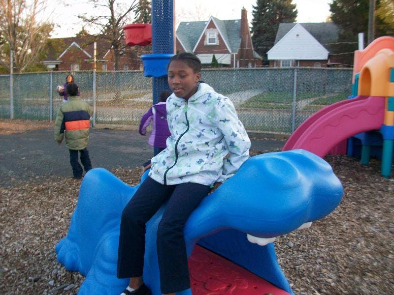Teen sitting on a blue spring rider at a playground