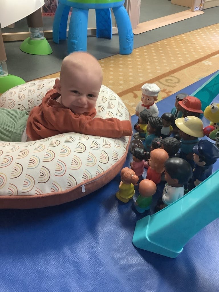 Child in a rainbow-patterned baby support pillow next to toy figures