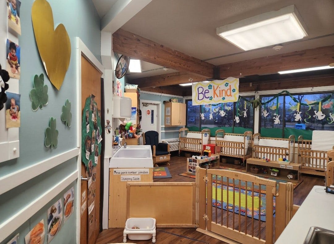 A colorful daycare room with several wooden cribs and a changing table
