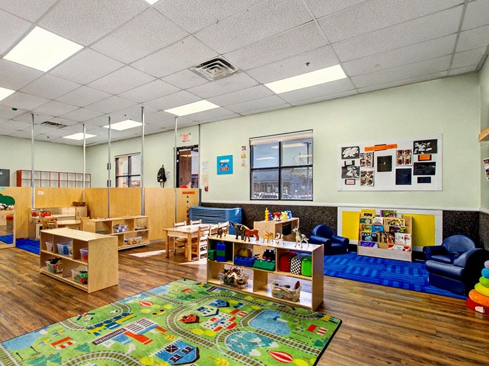 An empty children's classroom with play areas, furniture, and a rug