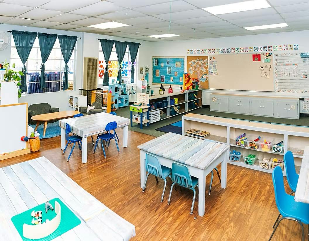 Empty preschool classroom with small tables and chairs and storage shelves