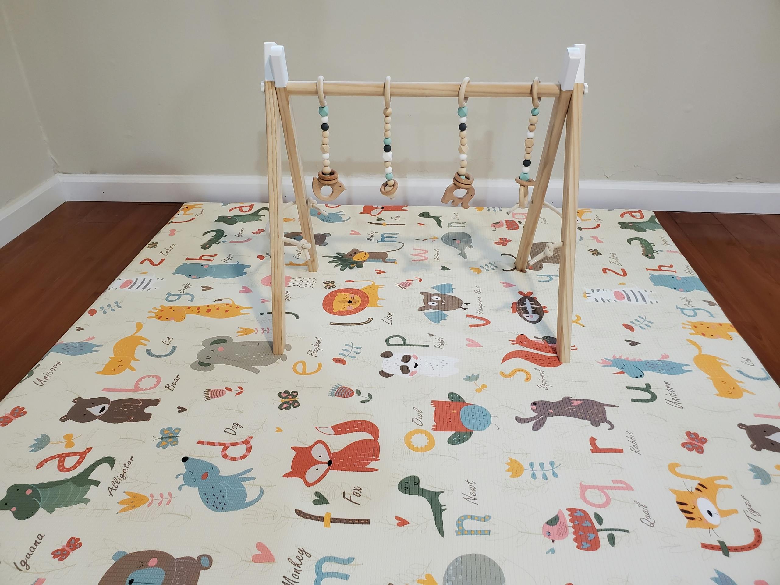 Wooden baby gym with hanging toys over a play mat with animal illustrations