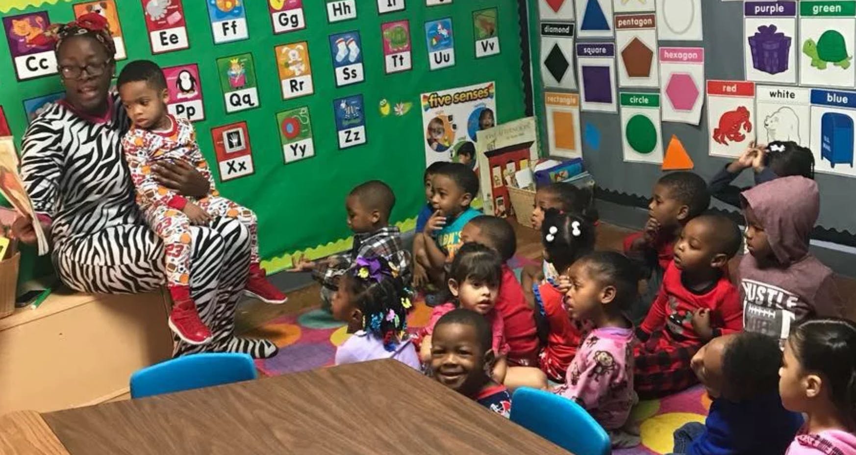 Person holding a child in a classroom with other children sitting on the floor