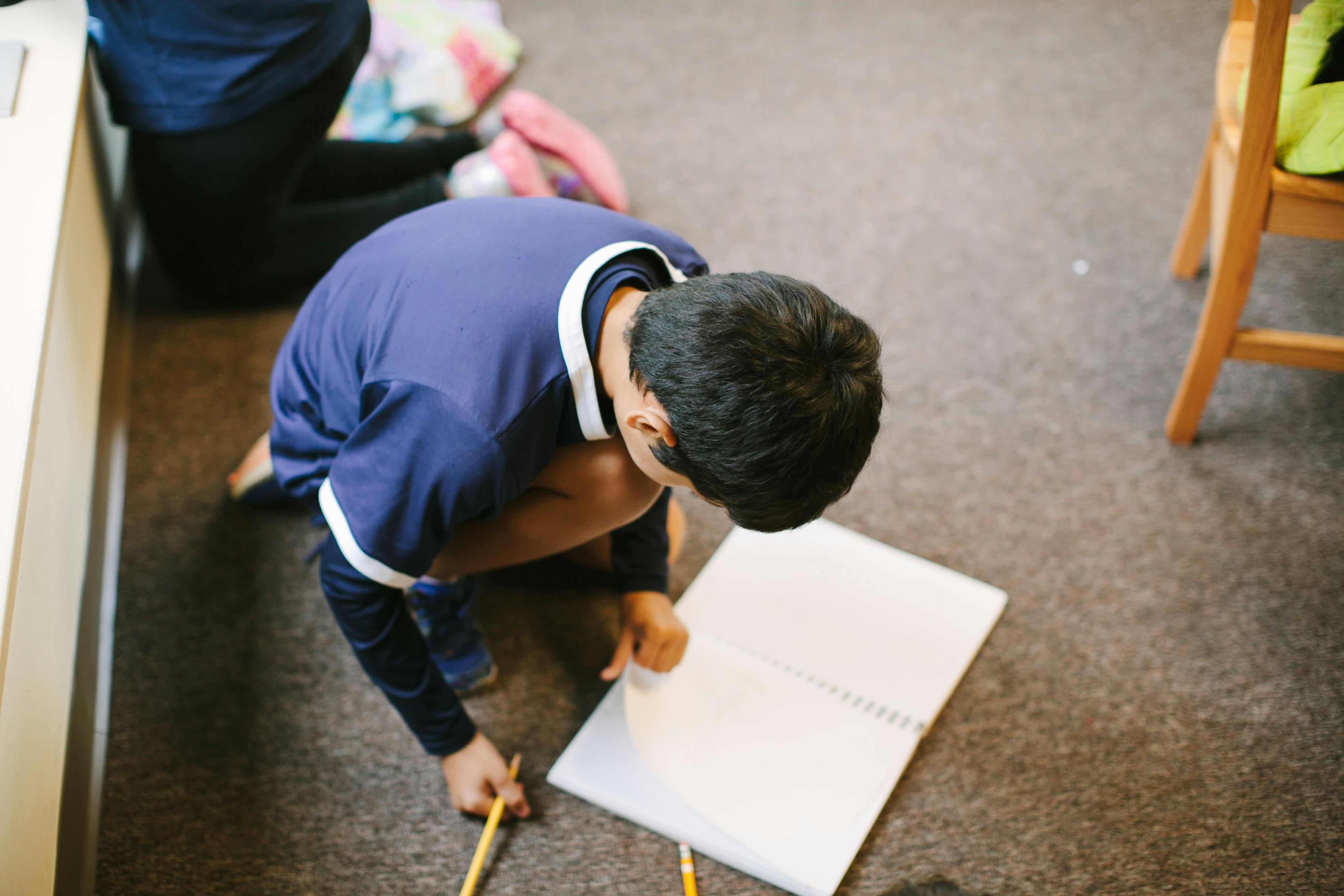 Child kneeling on floor drawing on paper