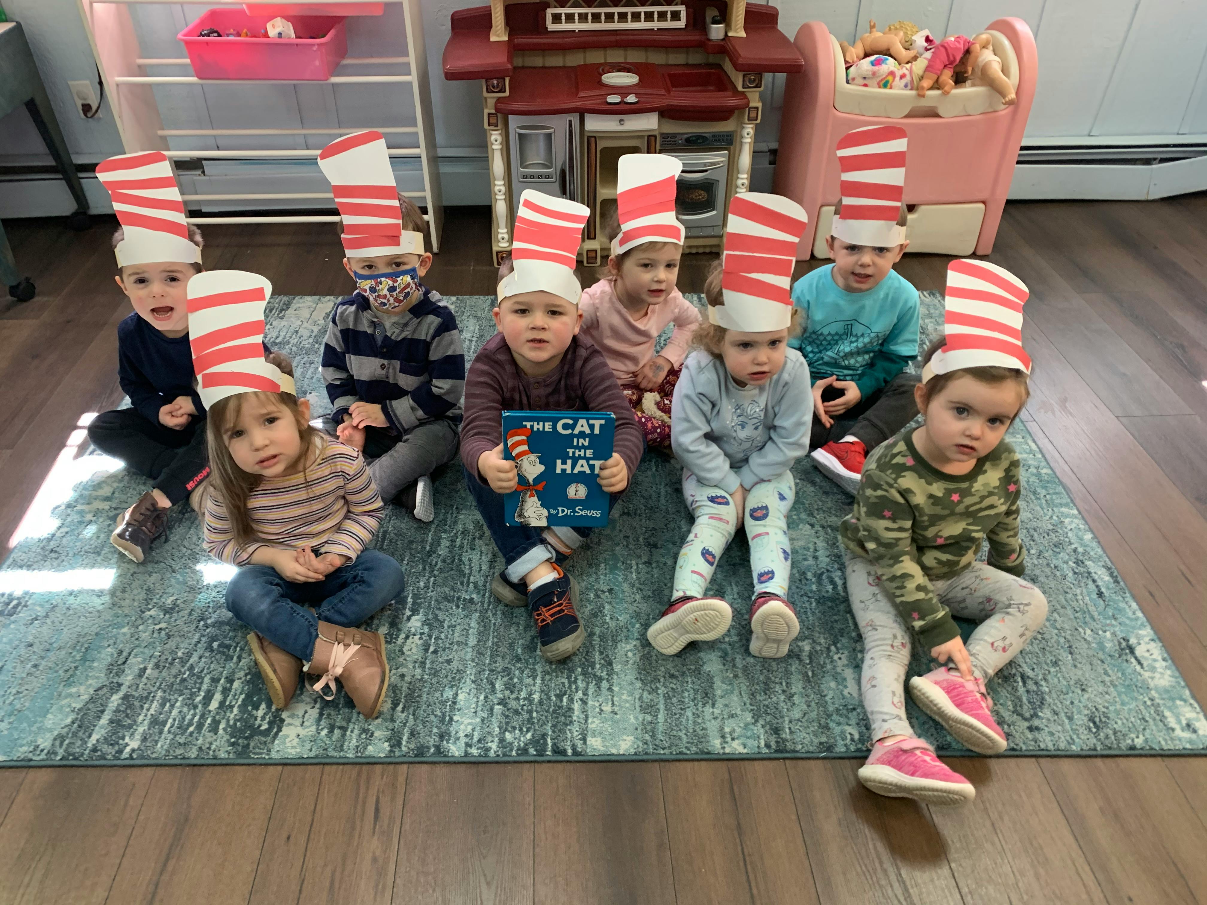 Group of children wearing striped hats, one holding a book titled "The Cat in the Hat"