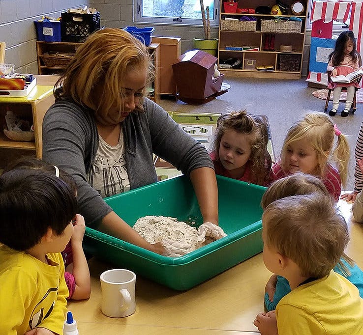 Adult and children kneading dough in a green bin in a classroom