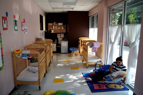 Person sitting on floor next to cribs in a room