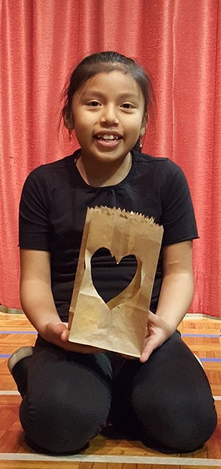 Child kneeling and holding a paper bag with a heart cut out