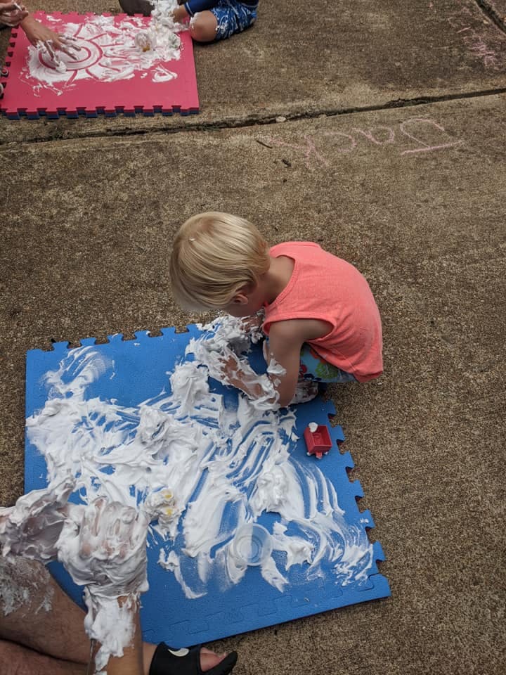 Child playing with shaving cream on a blue mat