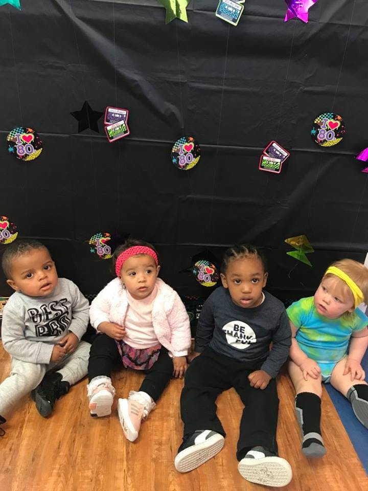 Four children sitting on a wooden floor in front of a black backdrop