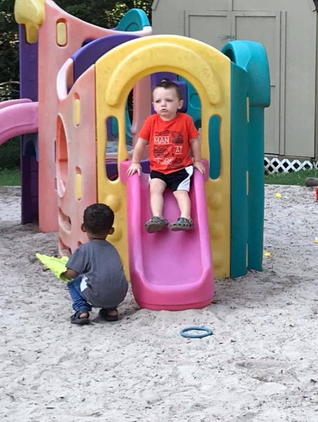 Two children on a playground, one on a slide and one crouching