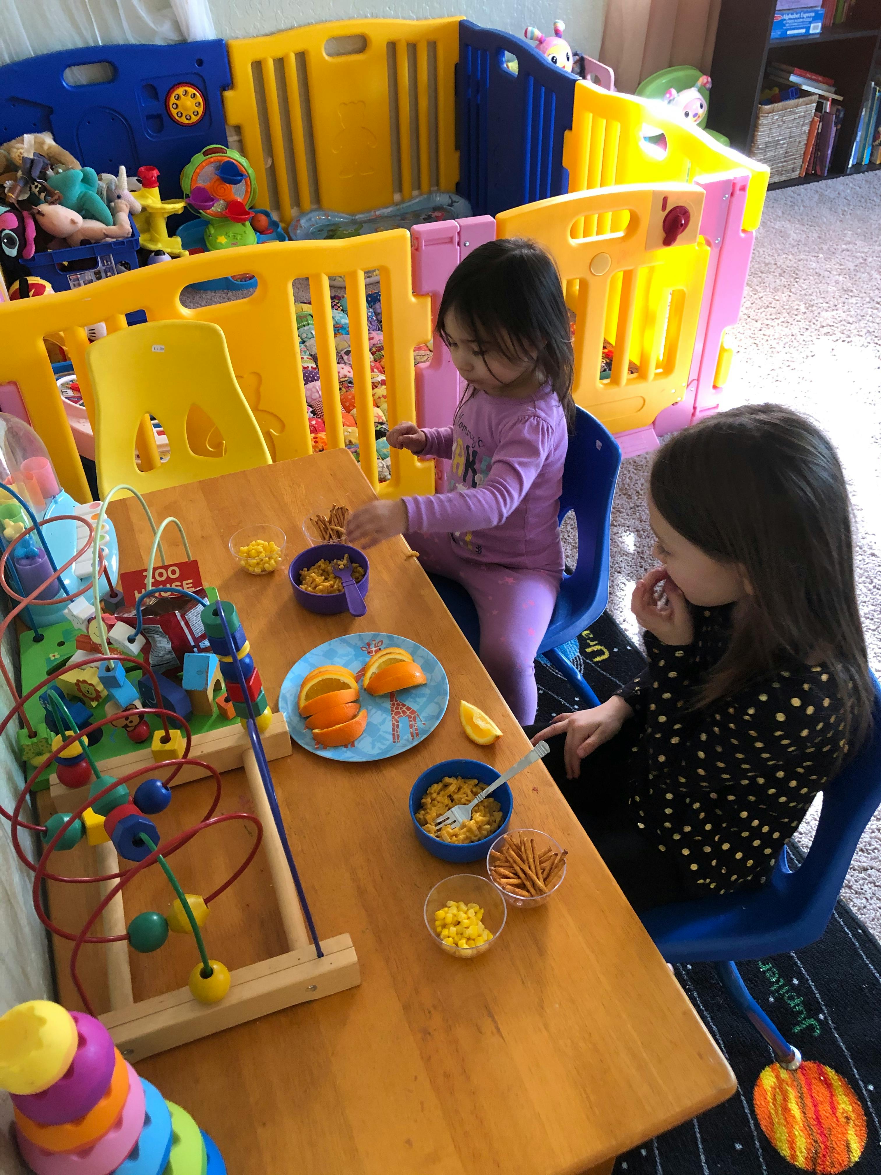 Two children sitting at a table with snacks and toys