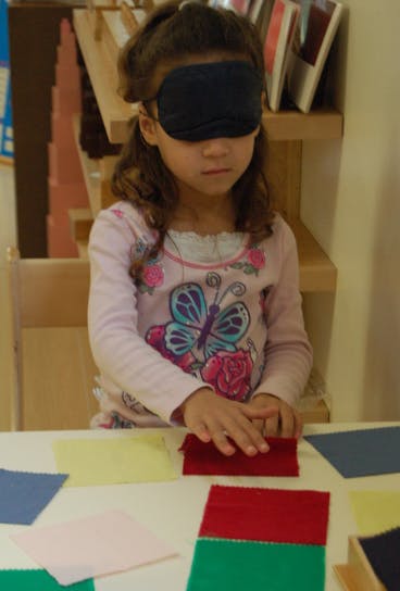 Child blindfolded touching fabric swatches on a table