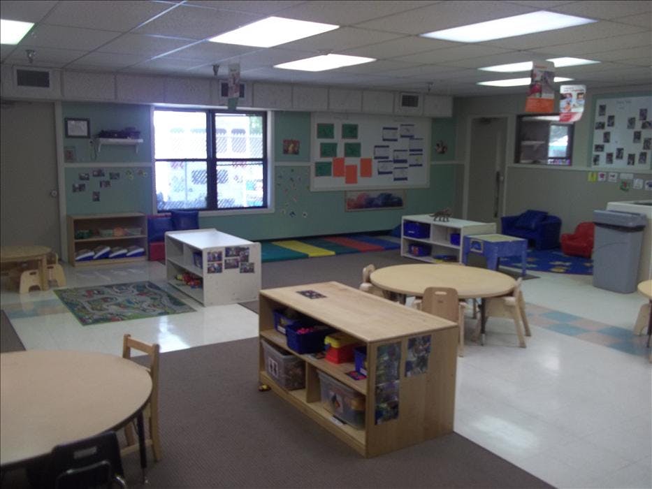 Empty classroom with small tables, chairs, and shelves with toys