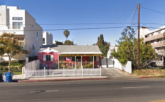 Small red building with a white picket fence in front of a larger white building