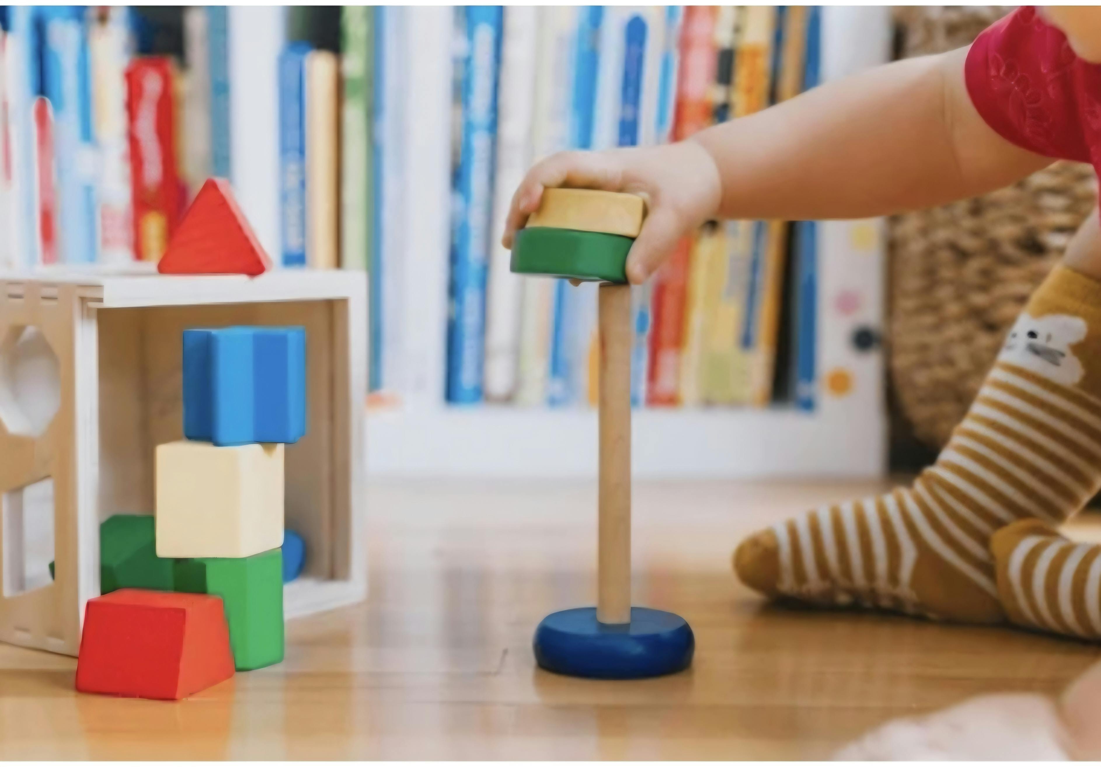 Child placing a green and yellow ring on a stacking toy
