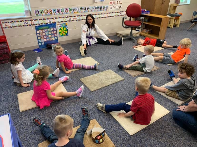 Adult and children sitting on floor stretching in a classroom