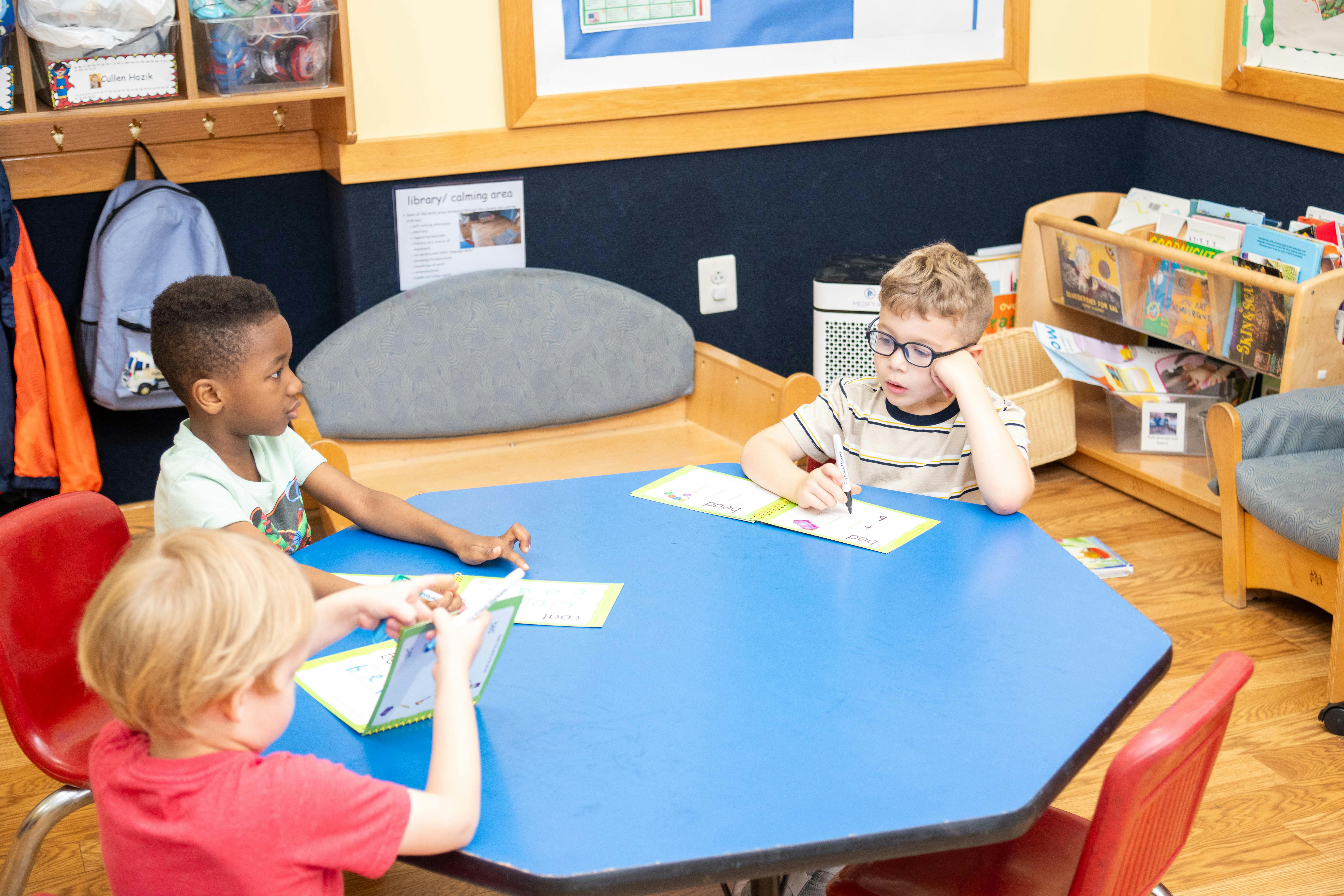 Three children sitting at a blue table in a classroom