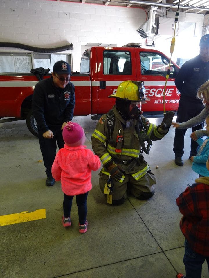 Firefighter kneeling in front of children with another person standing nearby