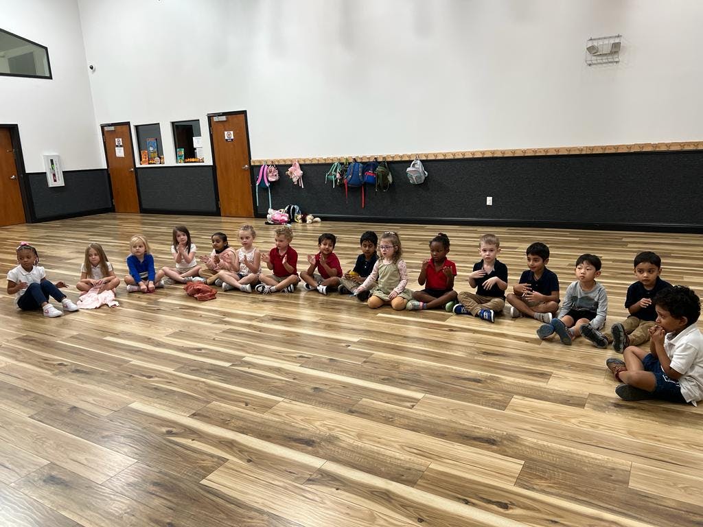 Children sitting on a wooden floor in a line