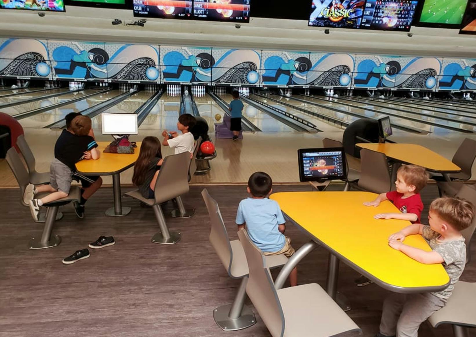 Children bowling and sitting at tables in a bowling alley