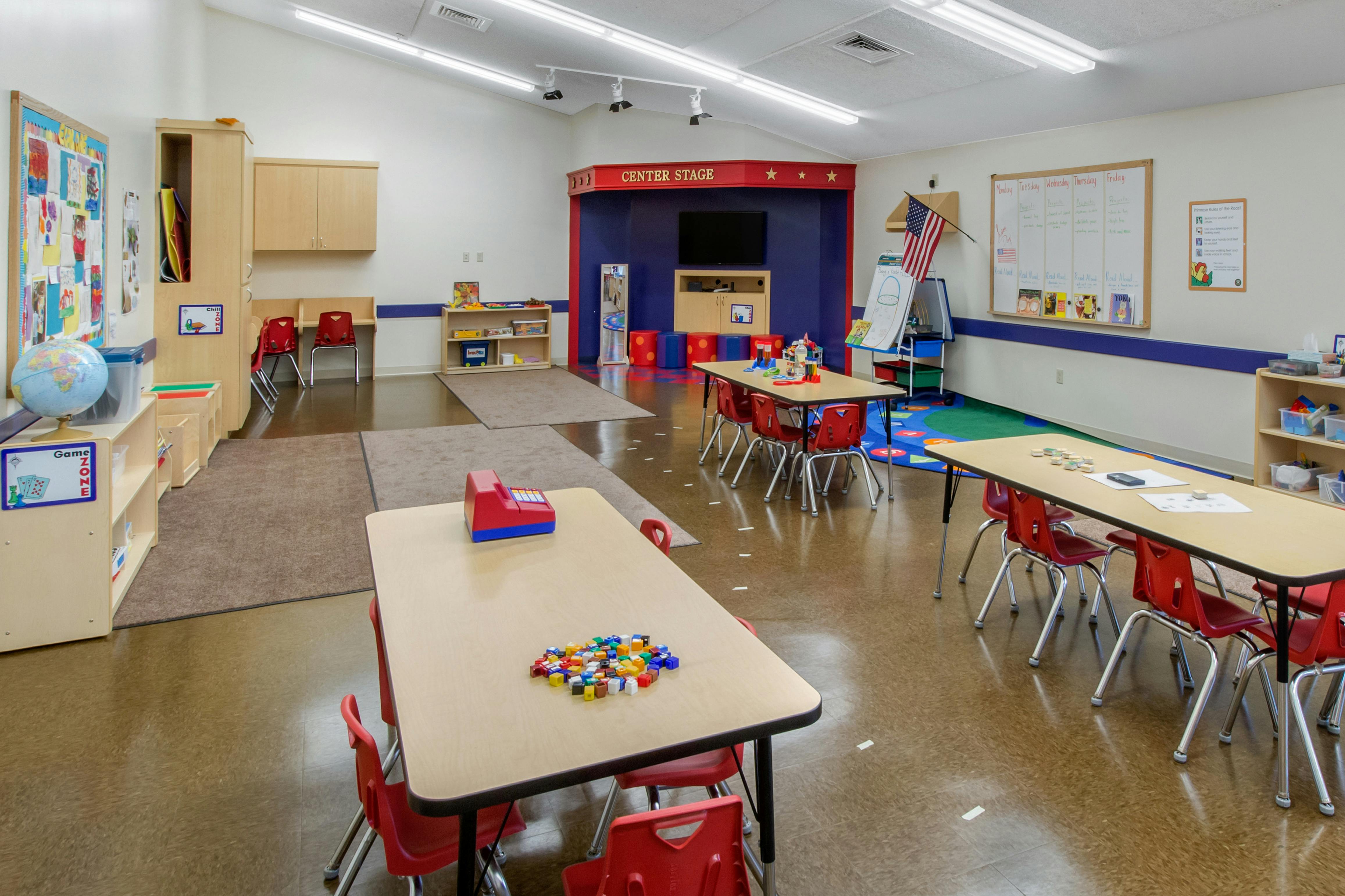 An empty classroom with tables, chairs, bookshelves, and a 'Center Stage' area