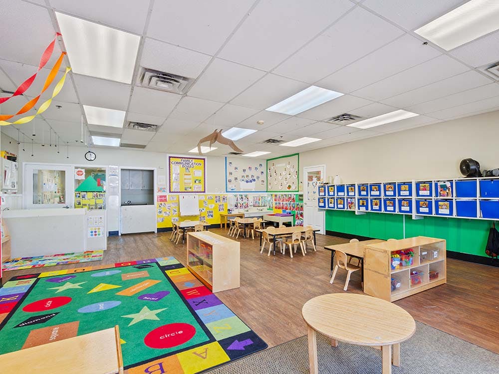 Colorful preschool classroom with small tables, chairs, and learning rug