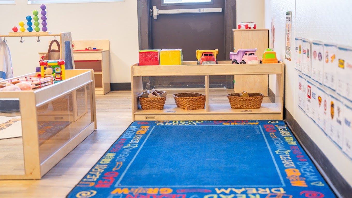 Toys on wooden shelves and a play rug in a classroom