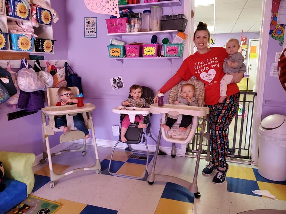 Person holding a child, with four other children in high chairs