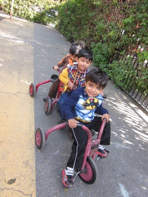 Three children riding tricycles in a line