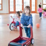 Child pushing a toy walker with other children in the background
