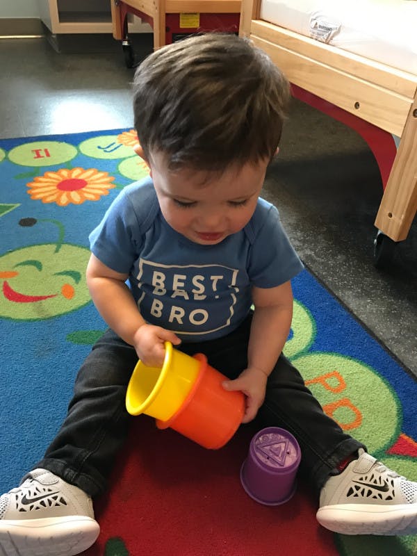 Child sitting on a rug, holding colorful stacking cups