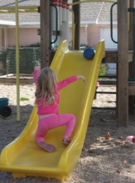 Child in pink climbing up a yellow slide with a blue ball