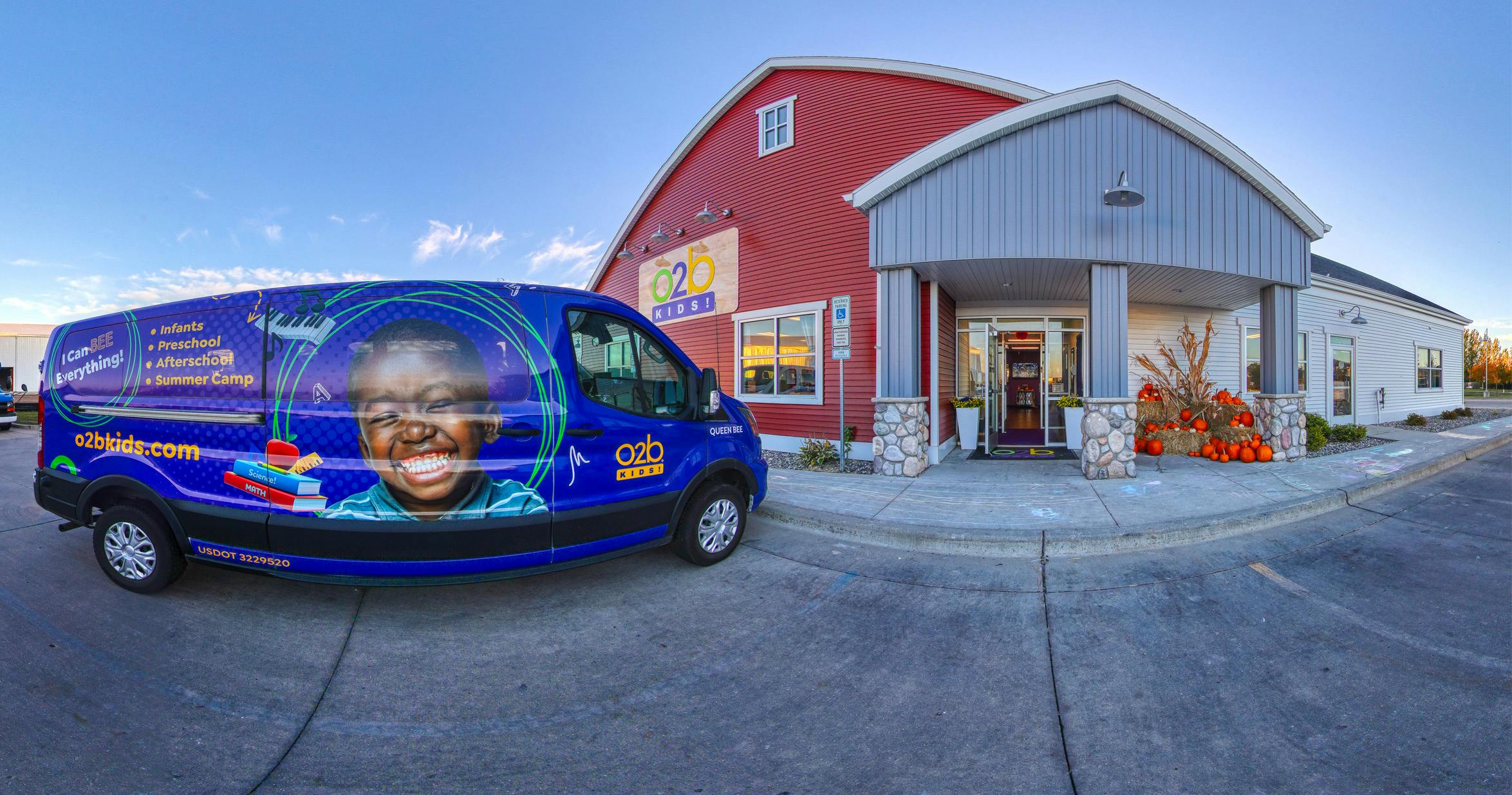A blue van with a child's face and text for "O2B Kids!" parked outside a building