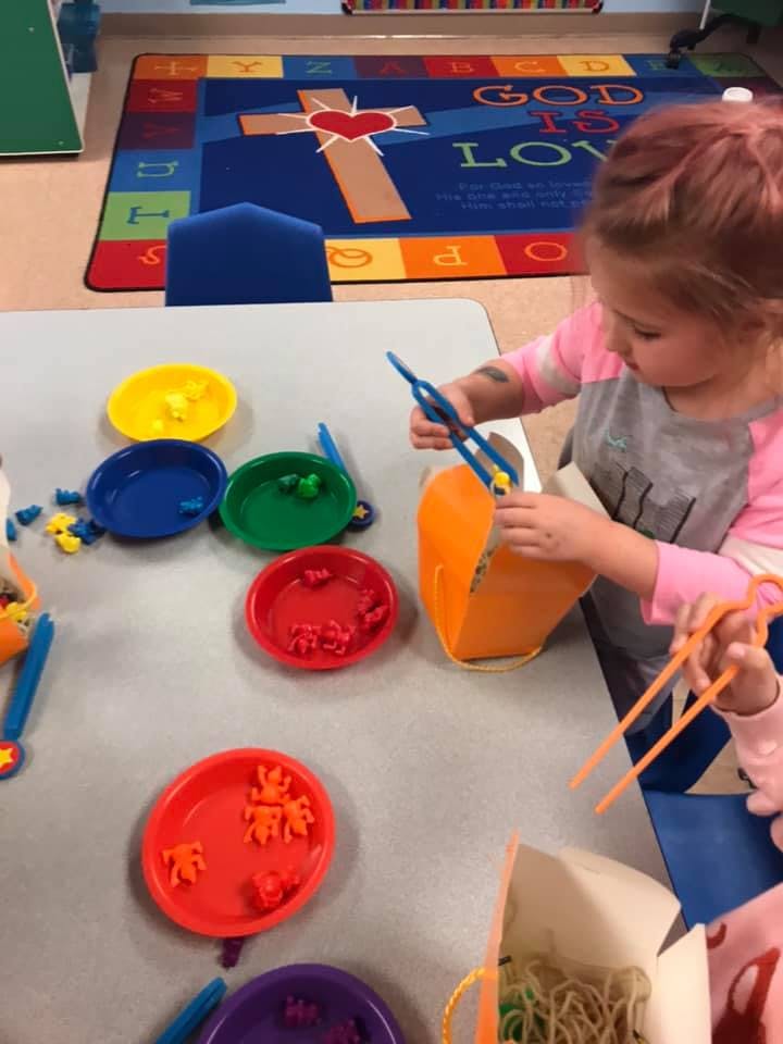 Child using tongs to pick up small objects from a container