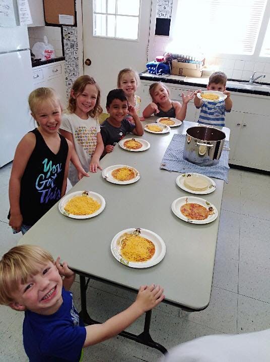 Multiple children standing around a table with plates of food