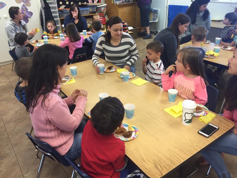 Adults and children sitting at tables with food and drinks