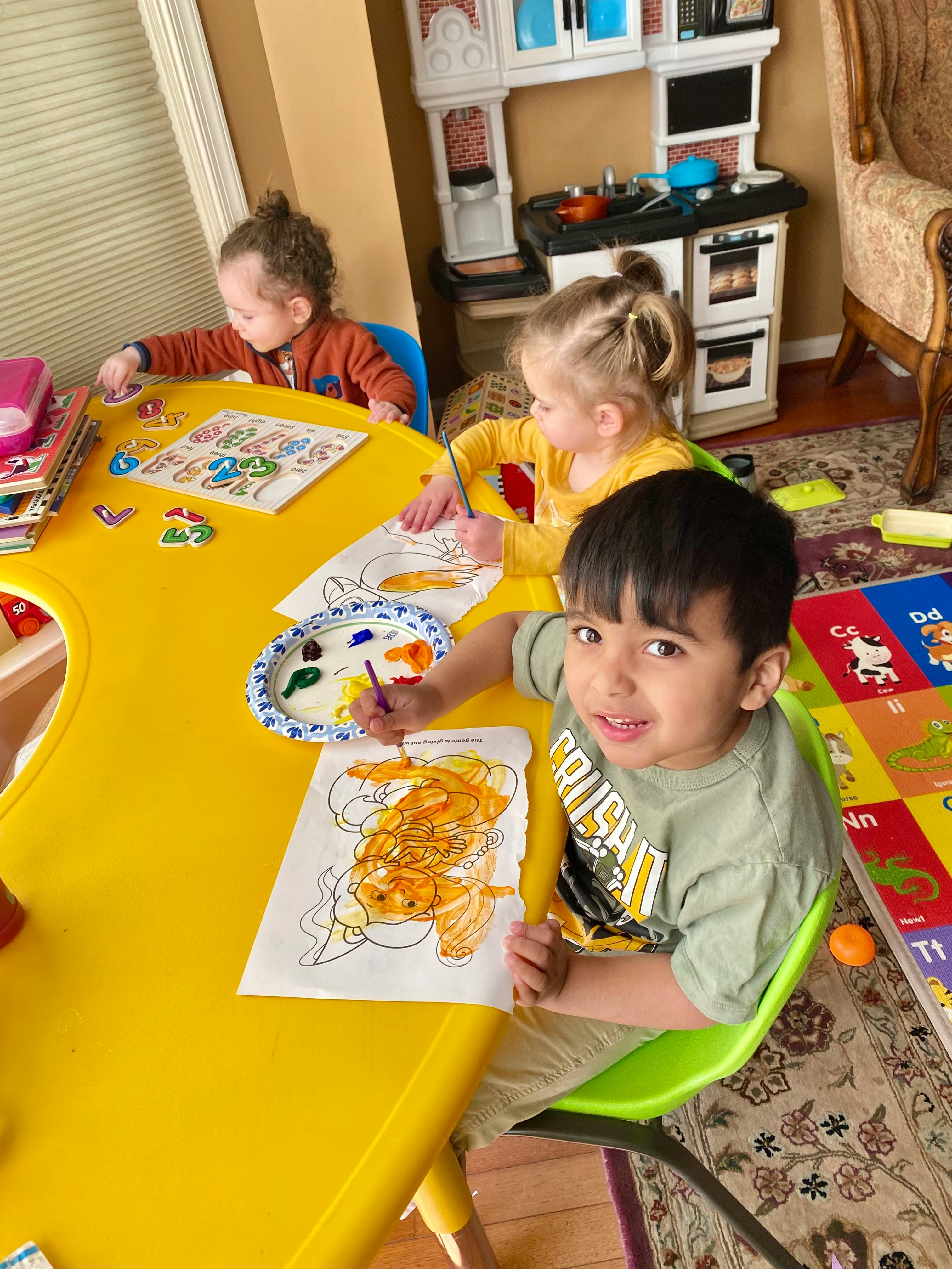 Three children painting at a yellow table