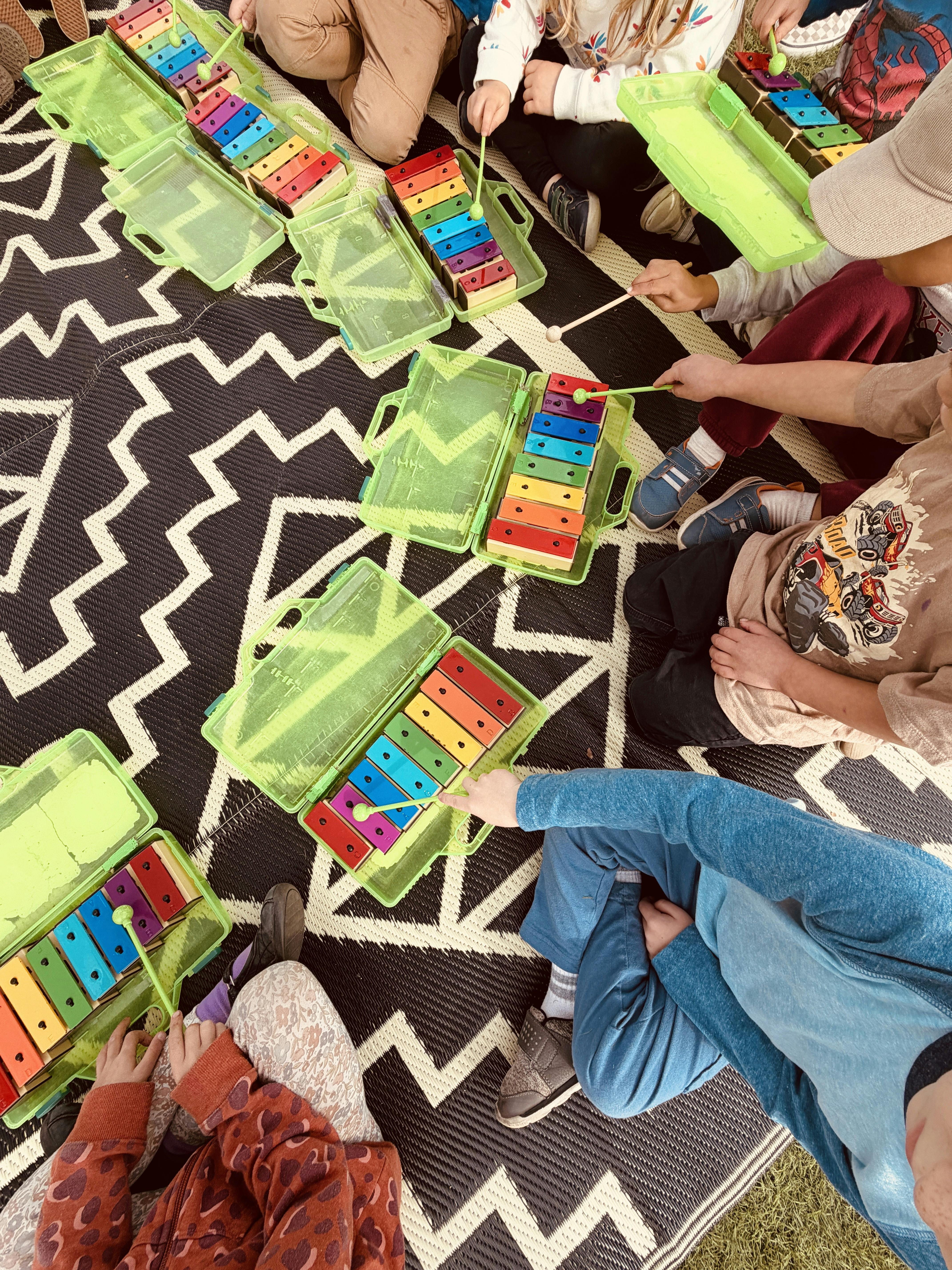 Children sitting on a patterned rug playing colorful xylophones