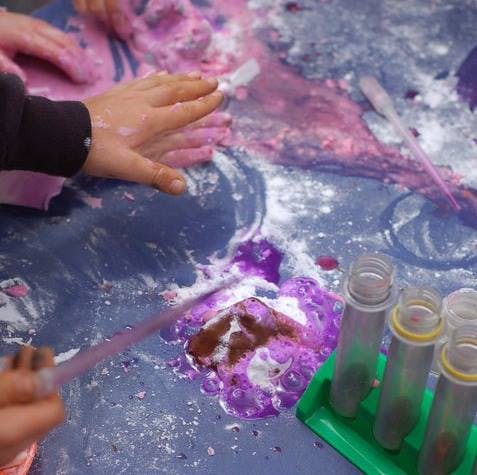 Child's hands mixing purple and pink slime on a blue surface