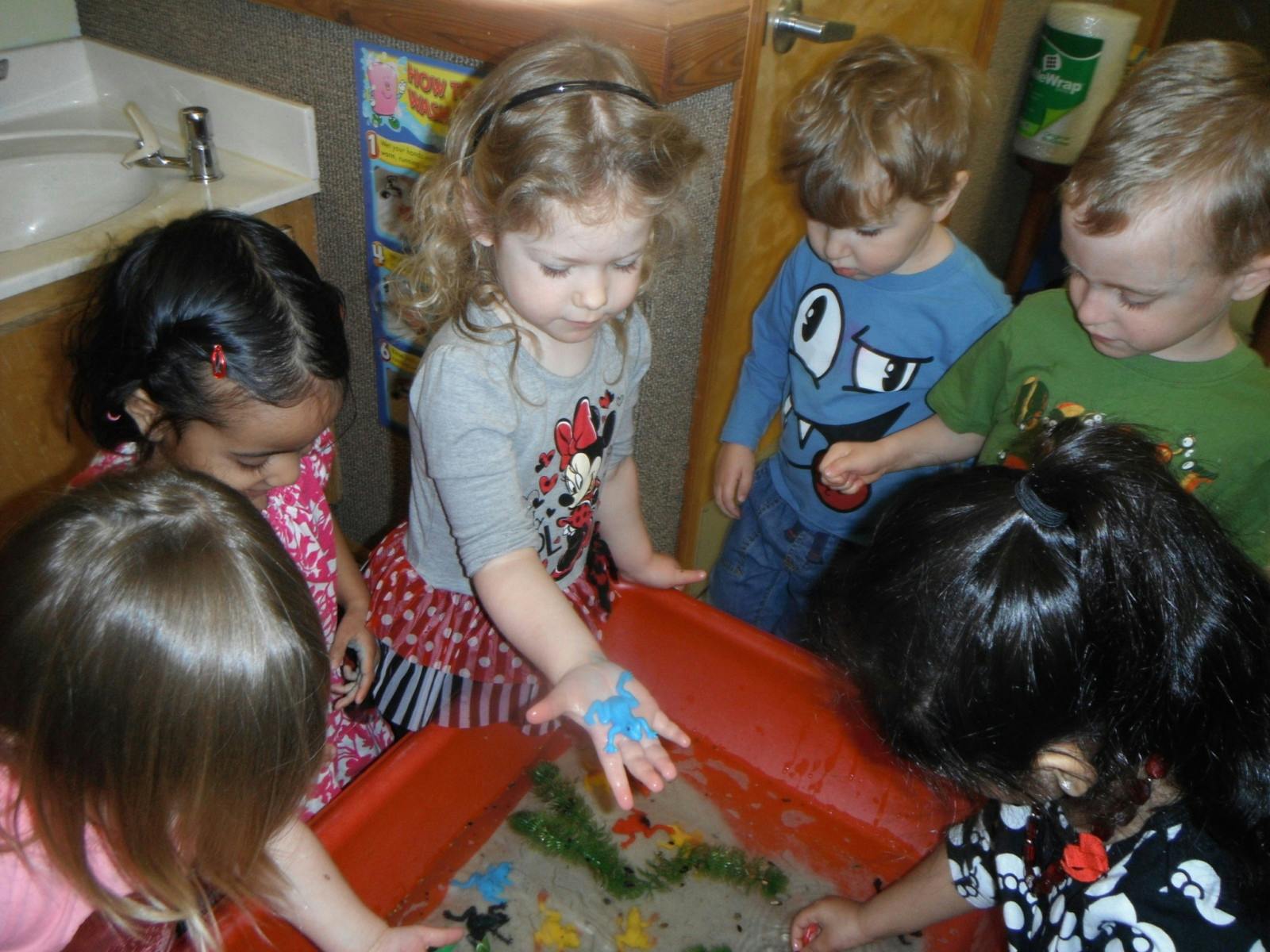 Children playing with sand and toys in a red sensory bin