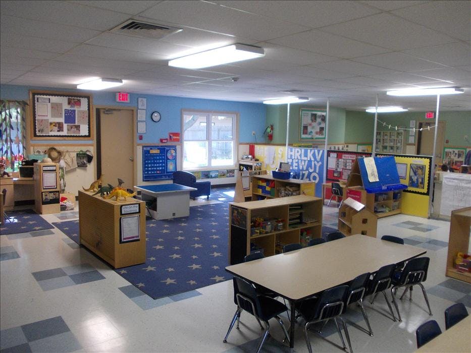 An empty early childhood classroom with tables, chairs, and play areas