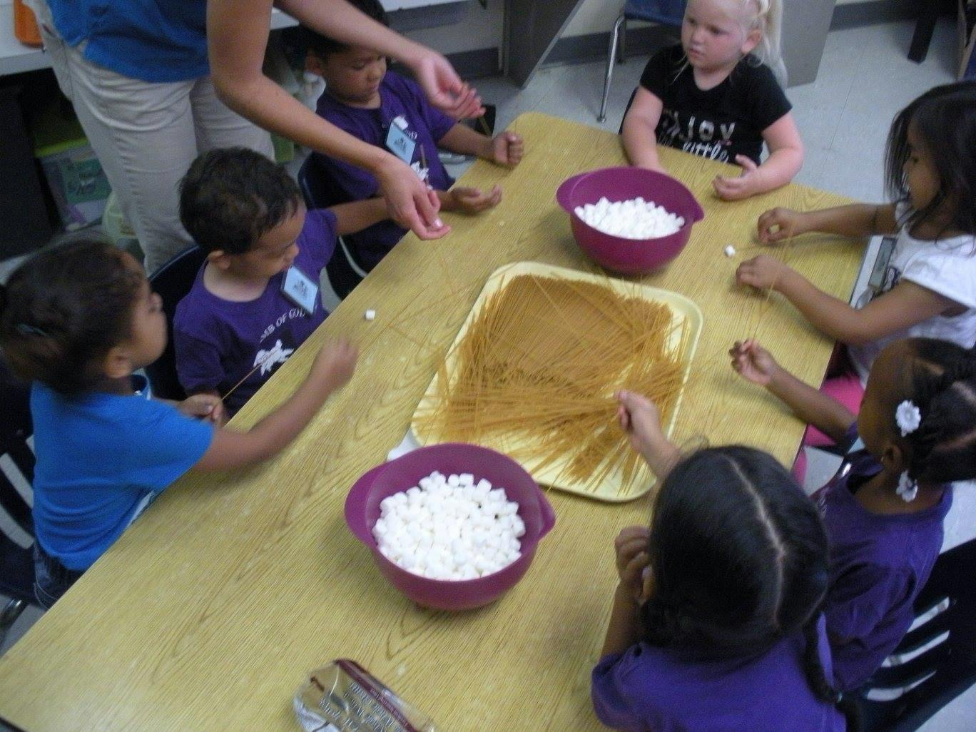 Adult and children at a table with bowls of marshmallows and spaghetti