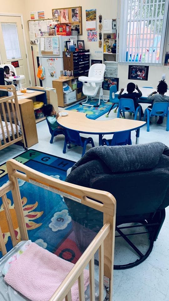 Children in a classroom with tables, chairs, and cribs